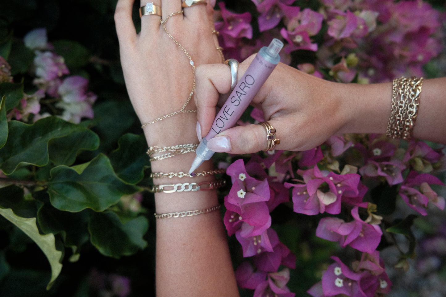 A wrist adorned with custom love saro permanent jewelry is using a cleaning pen to care for the 14K solid gold bracelets