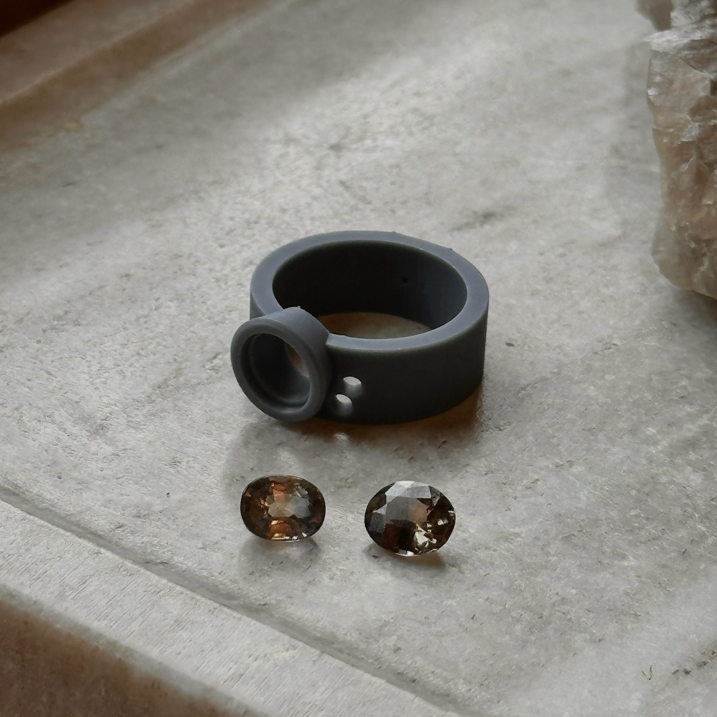 Gray silicone ring model with two Montana Sapphire center stones on a light stone surface