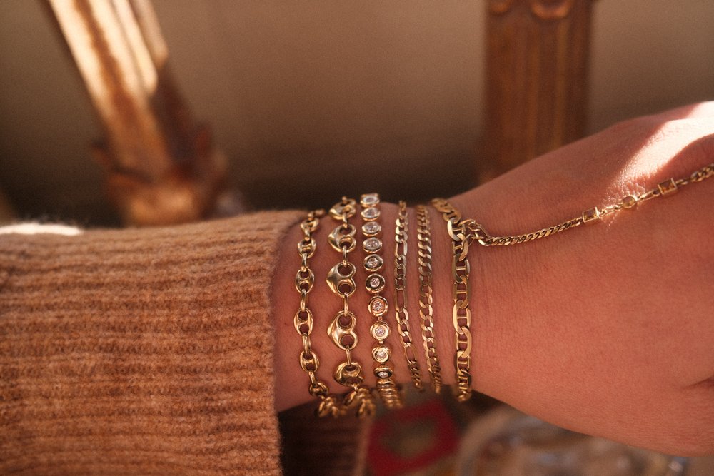 
                  
                    Stacked 14K solid gold bracelets with gemstone details on wrist, showcasing Love Saro’s luxury permanent jewelry collection
                  
                
