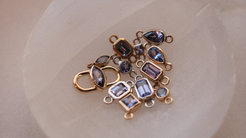 A quartz dish holds various tanzanite gemstones ready to be added to a customized piece of permanent jewelry
