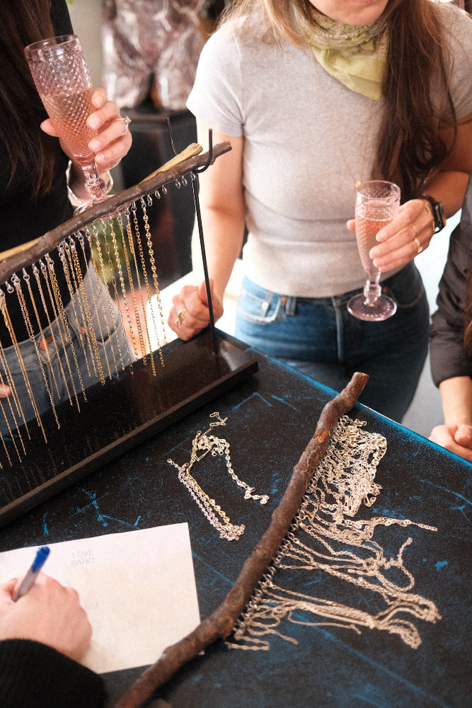 Guests sipping sparkling wine while choosing chains and charms for custom permanent jewelry at Love Saro Boulder.
